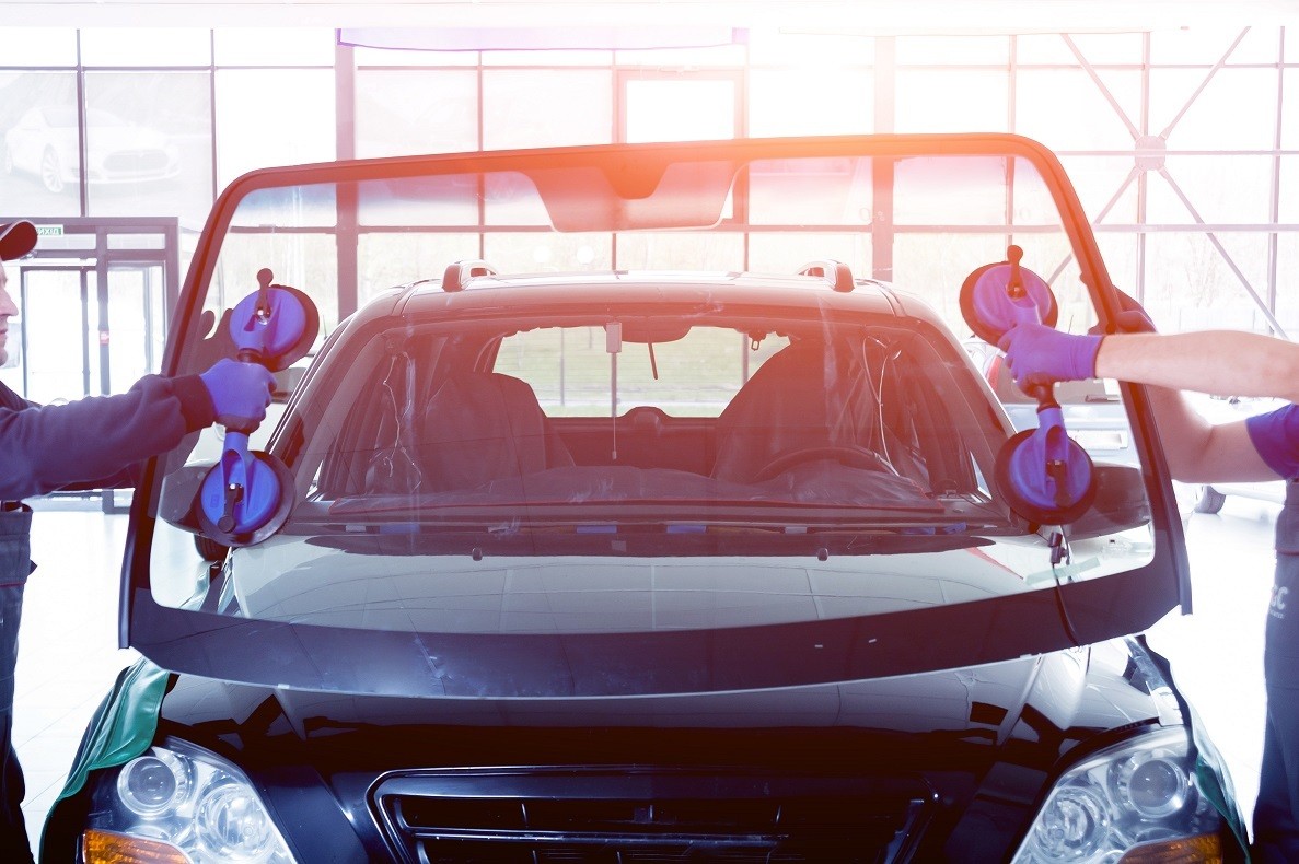 Automobile special workers replacing windscreen or windshield of a car in auto service station garage.